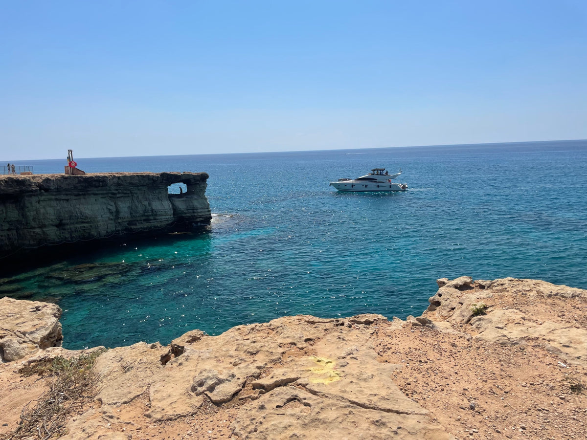 Yacht on clear blue sea beside a rocky coastal cove